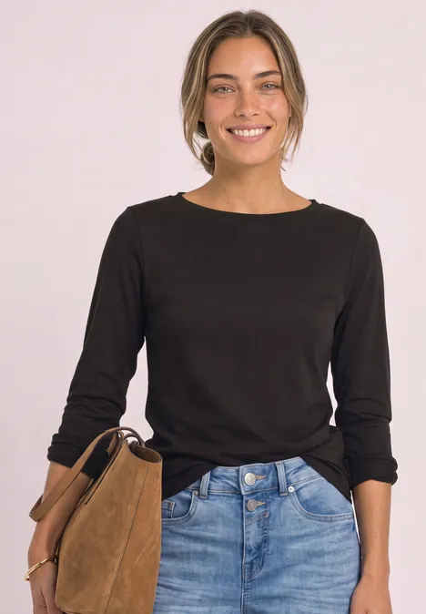 Langarm Shirt mit U-Boot-Ausschnitt black coffee Eine lächelnde Frau in schwarzem Langarmshirt und Jeans hält eine braune Wildledertasche vor hellem Hintergrund.