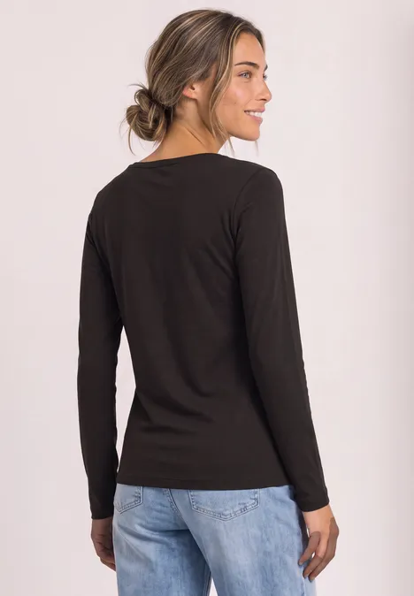 Langarm Shirt mit U-Boot-Ausschnitt black coffee Eine Frau in schwarzem Langarmshirt und blauen Jeans steht leicht seitlich, lächelnd.