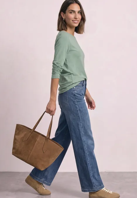 Femme en haut vert, jean large, sac marron et sandales sur fond clair.