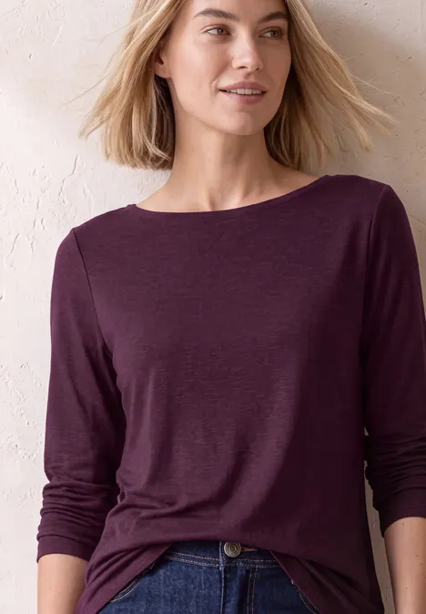 Langarm Shirt mit U-Boot-Ausschnitt berry maroon Frau mit blonden Haaren in dunkellila Langarmshirt vor hellem Hintergrund.