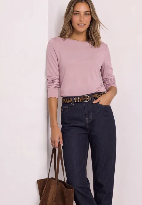 Femme en haut rose, jean bleu foncé, ceinture et sac marron.
