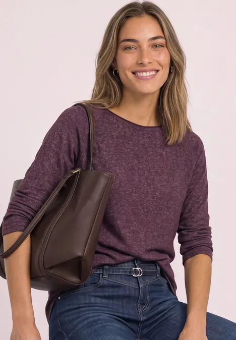 Femme souriante en pull violet décontracté et jean, portant un sac marron.