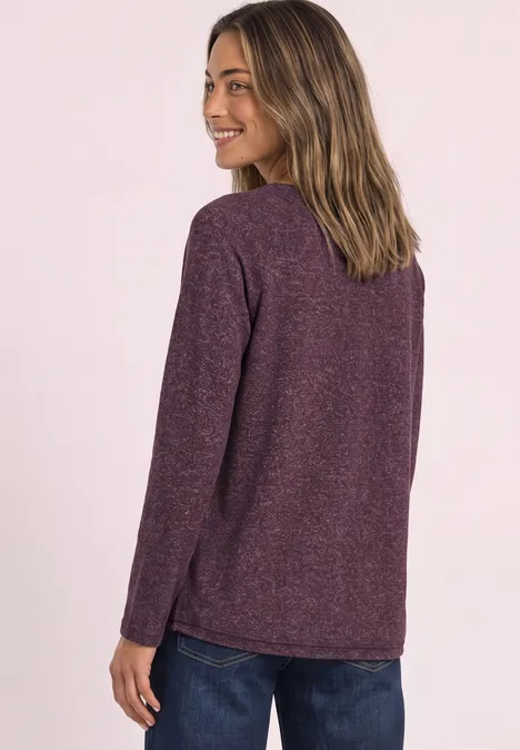 Femme de dos en pull violet, elle regarde par-dessus son épaule, sourire, fond clair.