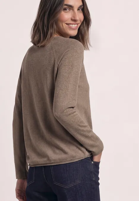 Femme en pull beige, souriant par-dessus son épaule.