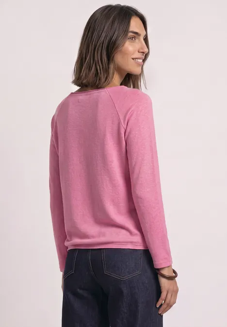 Eine Frau in rosa Pullover und blauer Jeans schaut über ihre Schulter.
