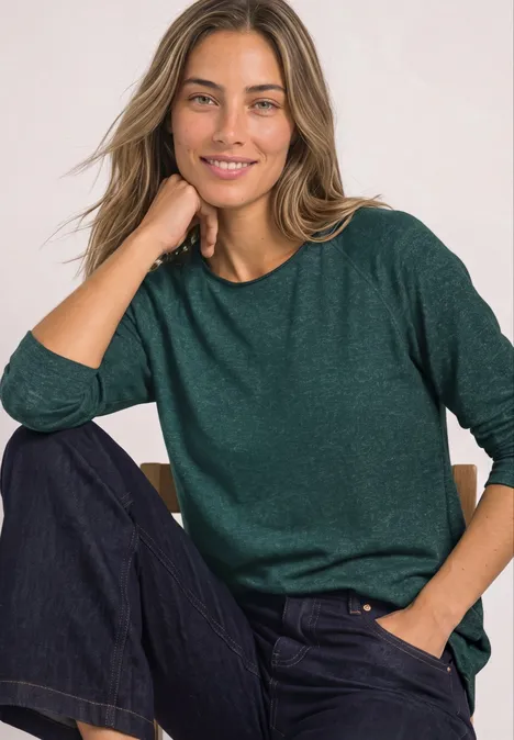 Langarm Shirt mit Rundhals und Rollkante shadow teal Lächelnde Frau im grünen Pullover und Jeans, sitzend und stützt das Kinn auf die Hand.