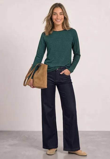 Langarm Shirt mit Rundhals und Rollkante shadow teal Frau in grünem Langarmshirt, weiten Jeans und beiger Tasche lächelnd vor neutralem Hintergrund.