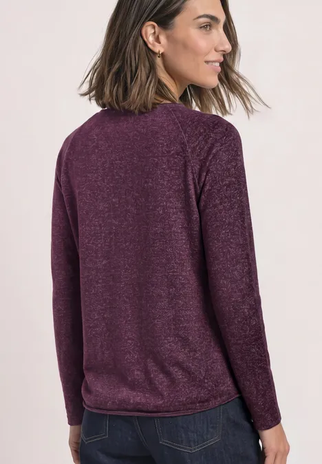 Eine Frau mit schulterlangem braunem Haar trägt einen violetten Pullover und blickt seitlich.