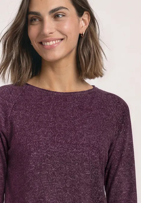 Eine junge Frau mit schulterlangem Haar trägt einen lila Pullover und lächelt leicht.
