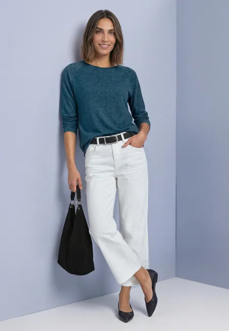 Frau im schicken Casual-Outfit: grünes Dreiviertelarm-Shirt, weiße Culottes, schwarze Ballerinas und große Tasche.