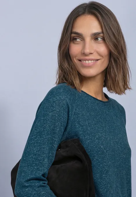 Eine Frau in grünblauem Pullover lächelt und schaut zur Seite.