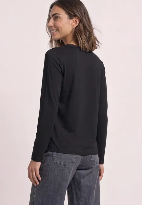 Une femme portant un haut à manches longues noir et un jean, regard par-dessus l’épaule.