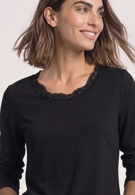Femme portant un haut noir à manches 3/4 avec bordure en dentelle au col rond.