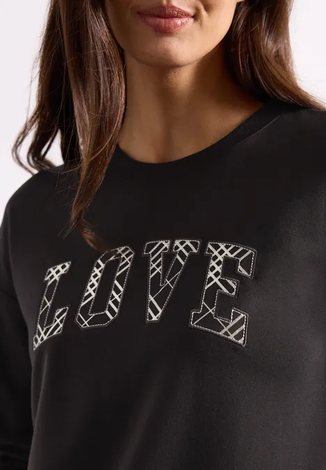 T-shirt à manches longues avec motif typographique black coffee Eine Frau trägt ein schwarzes Sweatshirt mit dem Schriftzug LOVE in weißem Grafik-Stil.