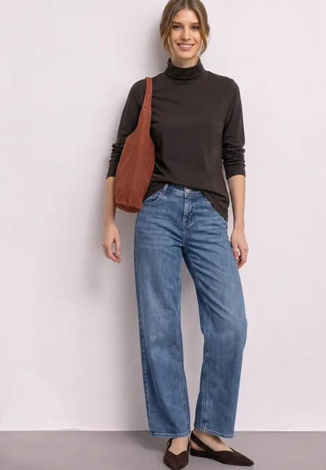 Frau mit schwarzem Rollkragen, blauen Straight-Jeans und brauner Schultertasche.