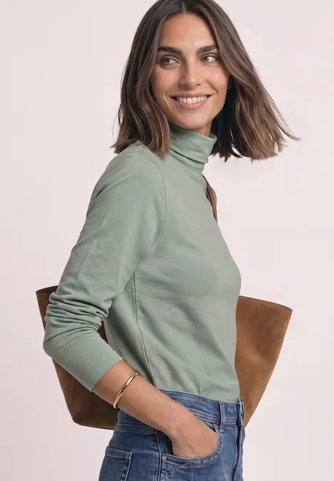 Langarm Shirt in Unifarbe mit Rollkragen eucalyptus green Eine lächelnde Frau in grünem Rollkragenpullover und Jeans, mit brauner Tasche über der Schulter.