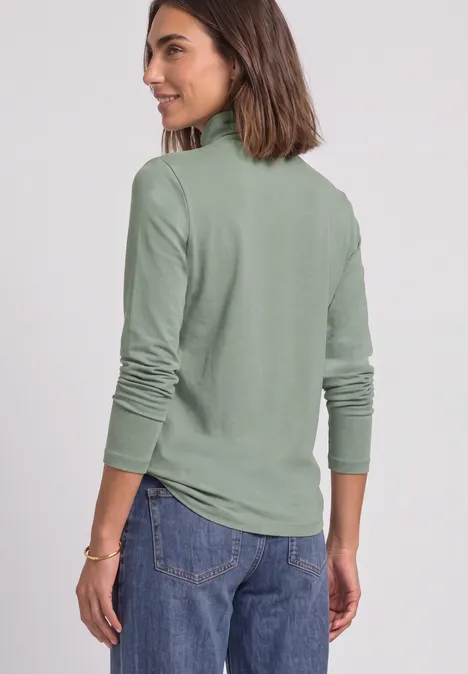 Langarm Shirt in Unifarbe mit Rollkragen eucalyptus green Frau in olivgrüner Rollkragenlongsleeve und Jeans, schaut lächelnd seitlich.