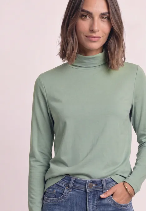 Langarm Shirt in Unifarbe mit Rollkragen eucalyptus green Frau mit schulterlangem Haar trägt grünen Rollkragenpullover und Jeans, eine Hand in der Tasche.