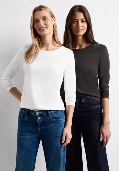 Zwei Frauen stehen nebeneinander, tragen Jeans und einfarbige Langarmshirts in Weiß und Schwarz.
