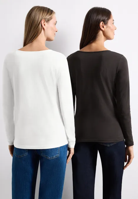 Zwei Frauen von hinten in langen Shirts (weiß und dunkel) mit Jeans, vor neutralem Hintergrund.
