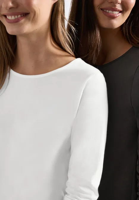 Zwei Frauen tragen schlichte Langarmshirts in Weiß und Schwarz.