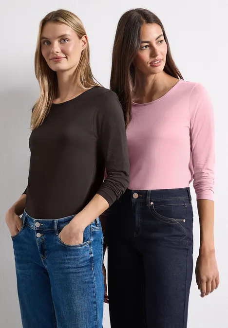 Zwei Frauen stehen nebeneinander, tragen lässige Langarmshirts und Jeans.