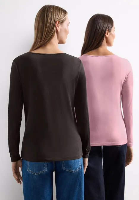 Zwei Frauen stehen Rücken an Rücken, tragen langärmlige Oberteile (schwarz, rosa) vor weißem Hintergrund.