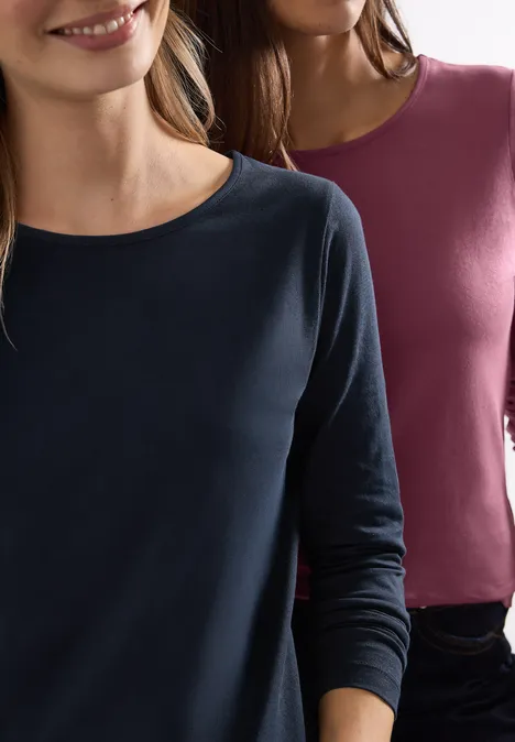 Zwei Frauen tragen langärmlige, schlichte Oberteile in Marineblau und Burgunderrot.