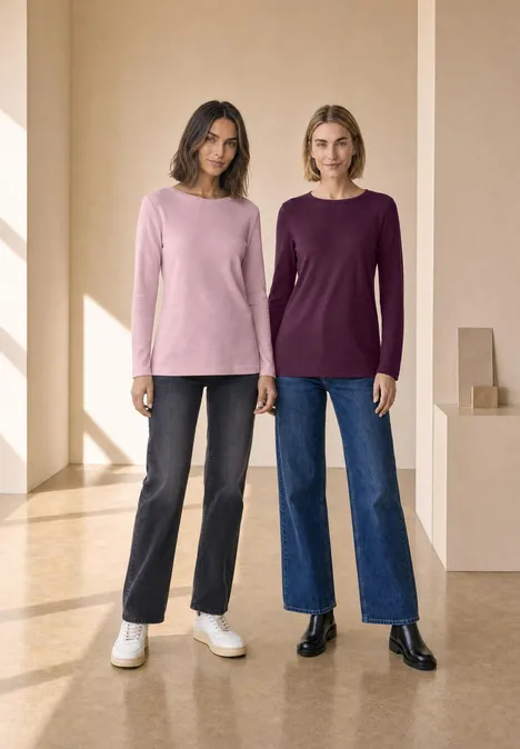 Zwei Frauen tragen ein rosafarbenes und ein dunkellila Langarmshirt vor hellem Hintergrund.