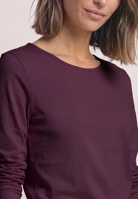 Frau mit bordeauxfarbenem Longsleeve, nur Oberkörper bis zum Kinn angeschnitten.