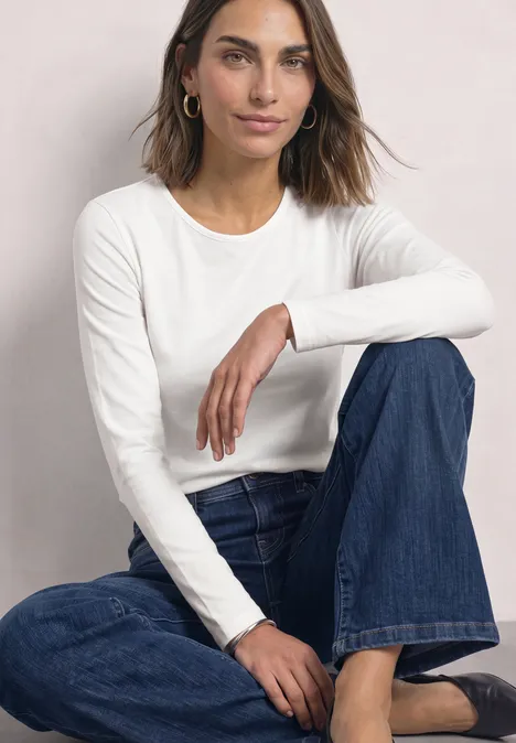 Langarm Shirts mit Rundhals im 2er-Pack off white/quiet rose Eine Frau sitzt lässig vor hellem Hintergrund, trägt weißes Langarmshirt und blaue Jeans.
