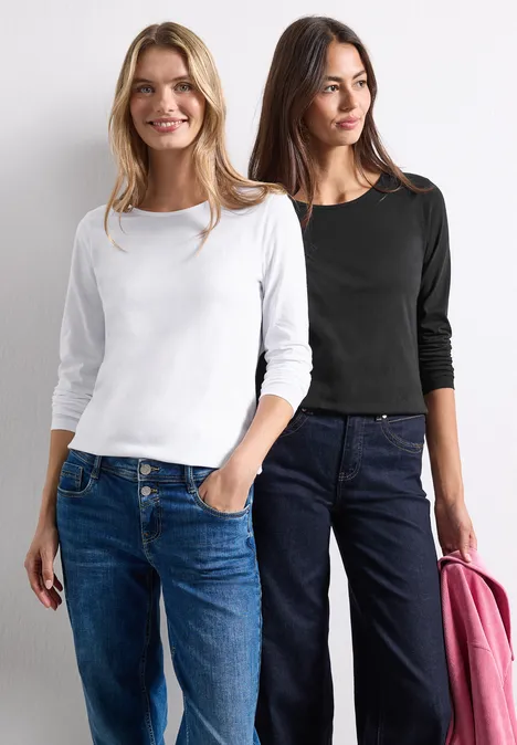 Zwei Frauen in Jeans, eine mit weißem, die andere mit schwarzem Oberteil und rosa Jacke, stehen nebeneinander.