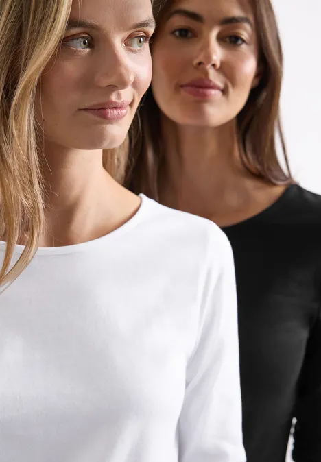 Zwei Frauen in schlichten Langarmshirts: vorne weiß, dahinter schwarz.