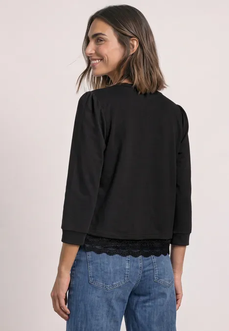 Frau in schwarzem Dreiviertel-Arm-Shirt und Jeans blickt lächelnd über die Schulter.