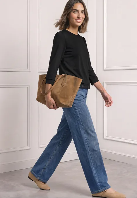 Frau trägt schwarzen Pullover, weite Jeans, beigen Schuhen und hält eine braune Tasche beim Gehen.