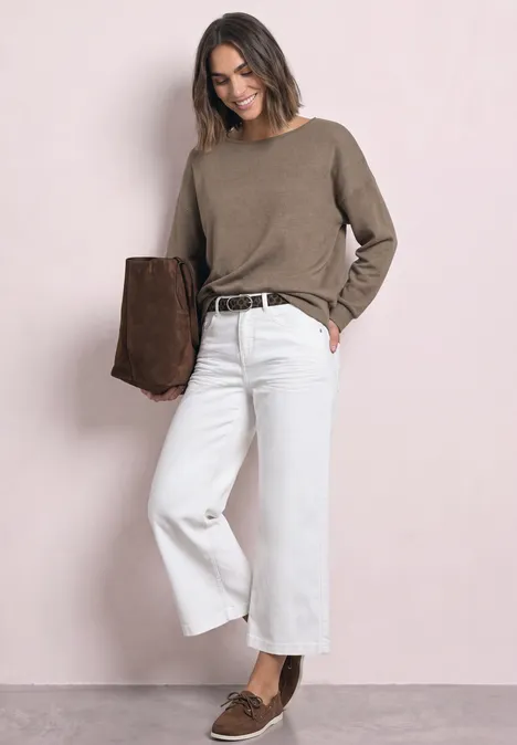 Femme en pull taupe, jean large blanc, mocassins bruns, portant une veste en daim marron.