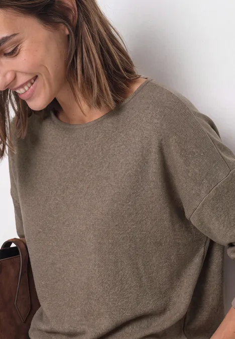 Femme souriante en pull ample kaki, tenant un sac marron, look décontracté.