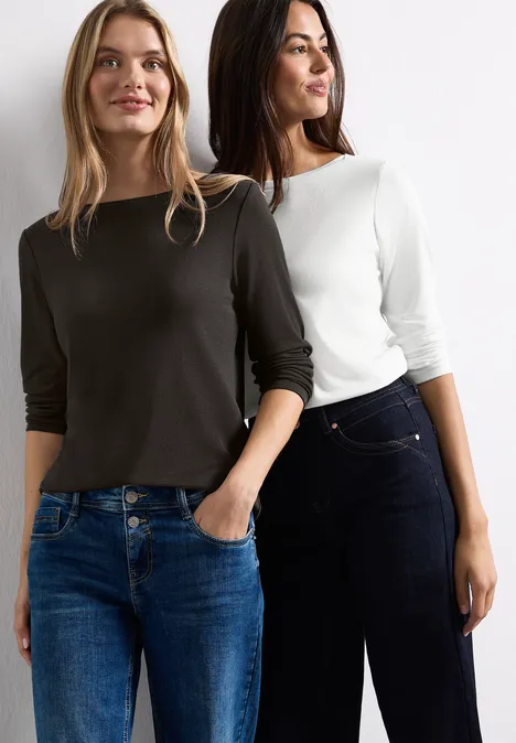 Zwei Frauen in Jeans und legeren Tops stehen nebeneinander und lächeln.