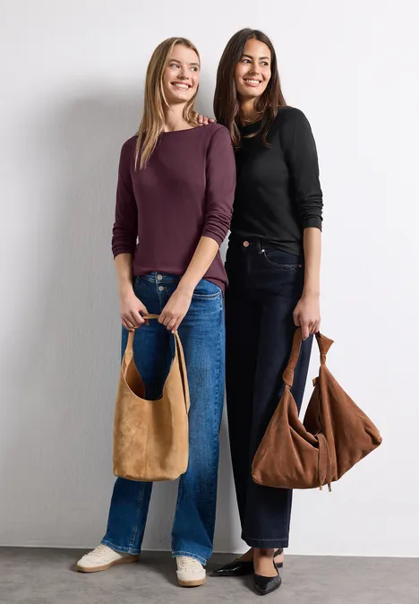 Zwei lächelnde Frauen in Jeans halten braune Taschen vor weißem Hintergrund.