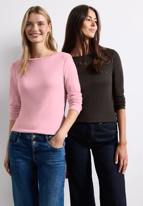 Zwei lächelnde Frauen in Jeans und Langarmshirts, eine in Rosa, eine in Schwarz.