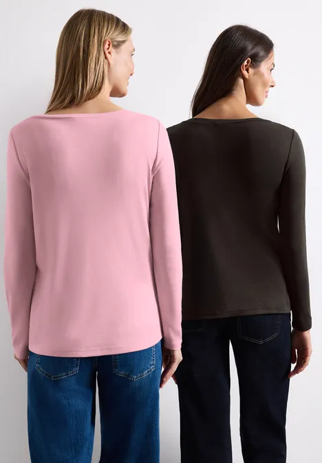 Zwei Frauen von hinten in schlichten Langarmshirts (rosa und schwarz) und Jeans vor weißem Hintergrund.
