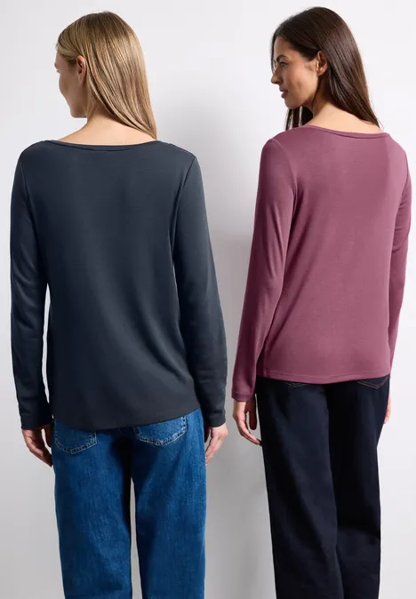 Zwei Frauen von hinten in legeren Outfits: eine in grauem Shirt und Jeans, eine in rotem Shirt und schwarzen Hosen.