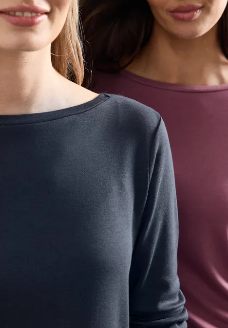 Zwei Frauen in schlichten Langarmshirts: eine in Dunkelgrau, die andere in Burgunderrot, nur Oberkörper sichtbar.