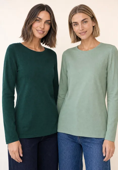 Zwei Frauen stehen nebeneinander und tragen langärmlige Pullover in dunklem und hellem Grün und Jeans.