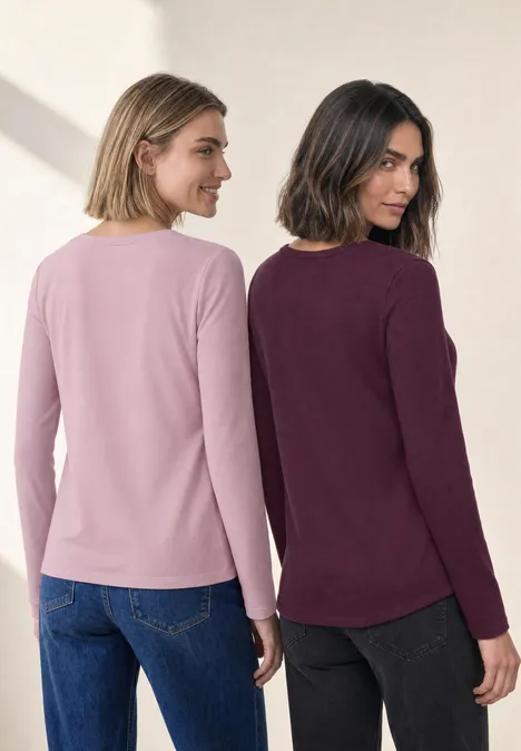 Twee vrouwen rug aan rug in shirts met lange mouwen, één lichtroze en de ander bordeaux.
