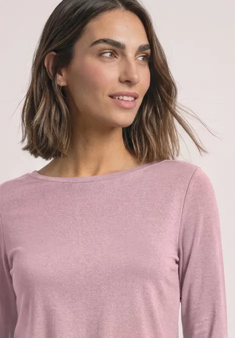 Eine Frau trägt ein lavendelfarbenes Langarmshirt mit rundem Ausschnitt.