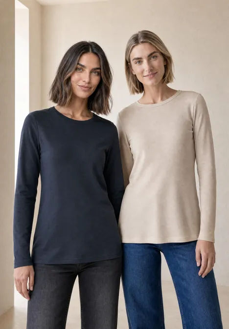 Zwei lächelnde Frauen in schlichten Langarmshirts (dunkelblau und beige) stehen nebeneinander.