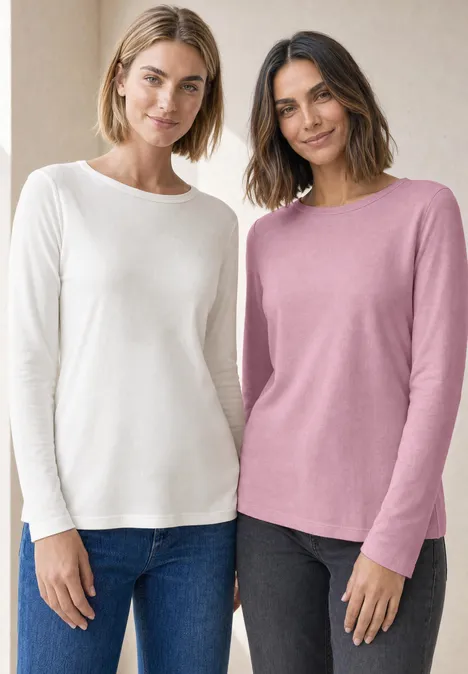 Twee lachende vrouwen in lange mouw truien (wit en roze) en jeans, tegen een neutrale achtergrond.