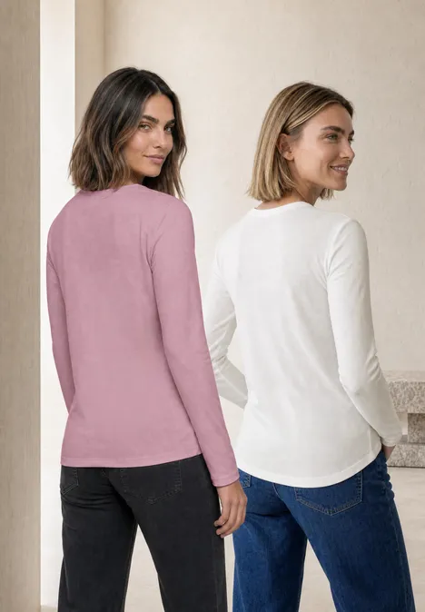 Twee vrouwen staan rug aan rug en dragen lange mouwen shirts in roze en wit met jeans.