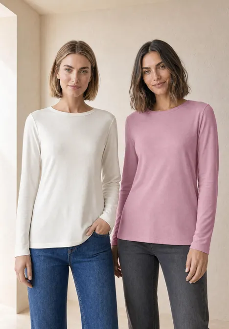 Twee vrouwen voor een lichte achtergrond dragen lange mouw shirts (wit & roze) met jeans en donkere broeken.